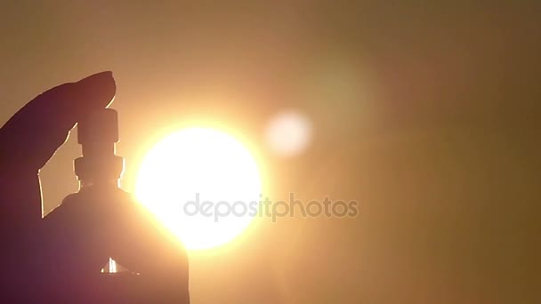 Kvinnlig Hand håller parfym och sprayer vätska på bakgrunden av en gyllene himmel — Stockvideo
