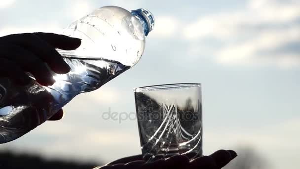 人は、澄んだ空の背景にあるガラスの中にボトルからきれいな水を注ぐ、手を見てクローズ アップ — ストック動画