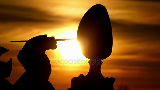 Silhouette of the Artist's Hands That Paints a Large Wooden Egg in Slow Motion on the Background of a Beautiful Sky — Stock Video