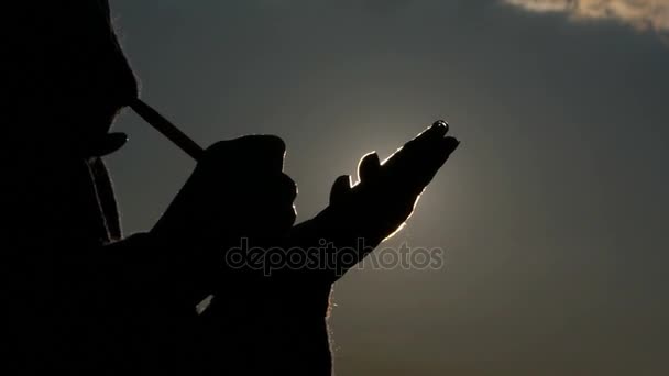 A Silhouette of a Person Writes in Notepad on the Background of the Sky, the Silhouette of Her Hands is Visible, the Sun Creates a Beautiful Backlight — Stock Video