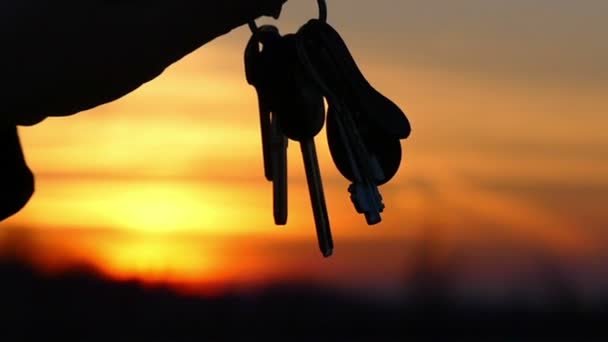 As chaves balançam lentamente na mão da pessoa contra o céu bonito, sua silhueta é visível — Vídeo de Stock