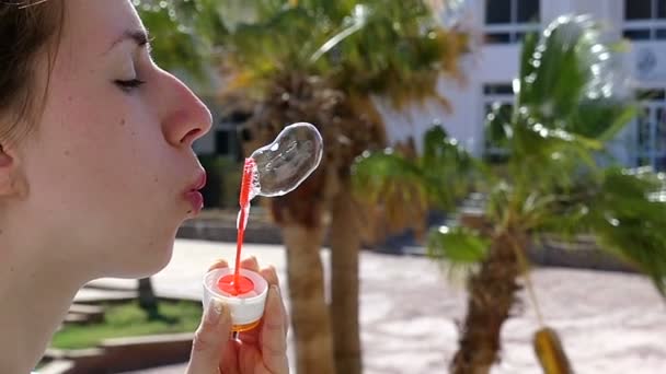 Mujer joven feliz está creando dos burbujas de jabón de fusión con una varita de jabón al aire libre — Vídeo de stock