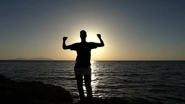 Mladý muž tance a ukazuje vysoké pět pozdrav na pláži při západu slunce v Slo-Mo — Stock video