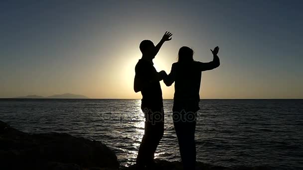 Un homme et une femme heureux agitent leurs mains sur un magnifique littoral au coucher du soleil à Slo-Mo — Video