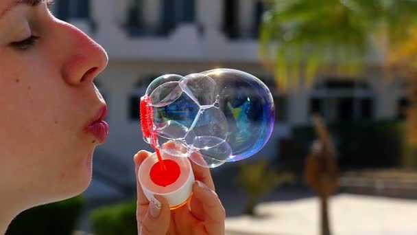 Mujer joven feliz está creando burbujas de jabón con una varita de jabón rojo al aire libre — Vídeos de Stock