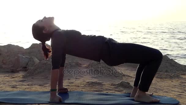Fiatal nő gyakorlatok jóga ászanák egy festői tenger partján, egy napsütéses napon — Stock videók