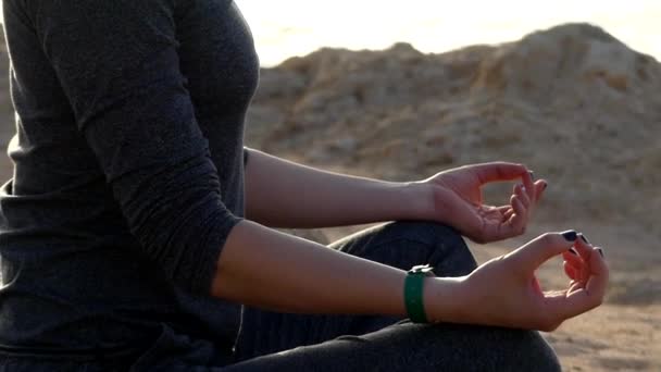 Mujer joven respira profundamente sentada en una esterilla de yoga en una postura de loto en un fondo marino con traje deportivo gris — Vídeo de stock