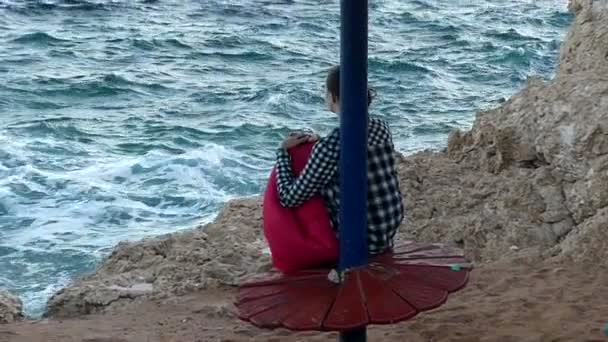 Drömmer ung kvinna sitter på en stenig havsstrand och leenden i Slo-Mo i sommar — Stockvideo