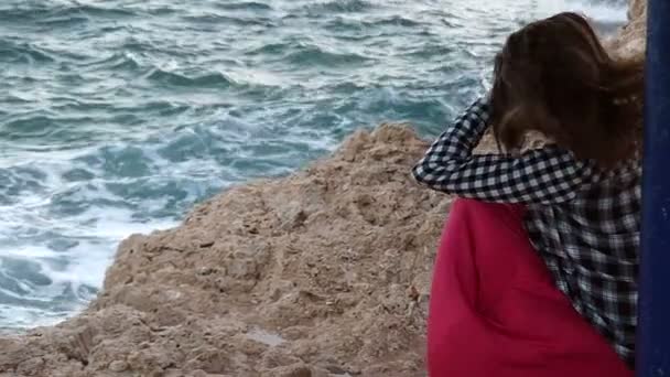 Atractiva jovencita se sienta en una costa rocosa y pone su cabello en orden en Slo-Mo en verano — Vídeos de Stock