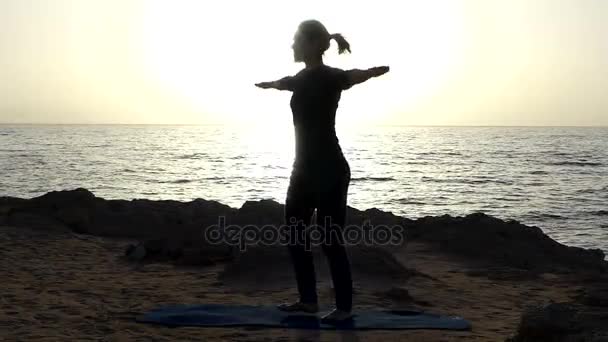 Mujer joven practica yoga Asana, dando la vuelta en una pintoresca orilla del mar en un día soleado — Vídeo de stock