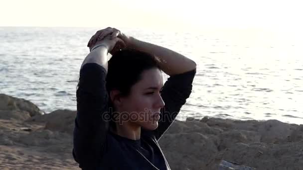 Slim Woman Passes Her Hand Over Her Head Sitting on a Yoga Mat on a Seabeach in Grey Sport Suit — Stock Video