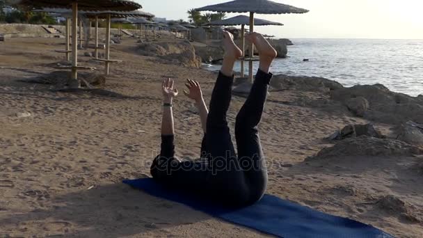 Νεαρή γυναίκα μεγάλωσε τα χέρια και τα πόδια ενώ ξαπλωμένος σε ένα χαλάκι γιόγκα στην παραλία στην Αίγυπτο — Αρχείο Βίντεο