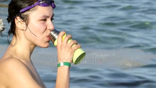 Веселая женщина в плавательных очках пьет чай из термоса и показывает пальцем вверх — стоковое видео
