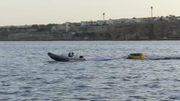 Caoutchouc bateau à moteur tire un canapé en caoutchouc et hôtels vus sur la côte montagneuse — Video