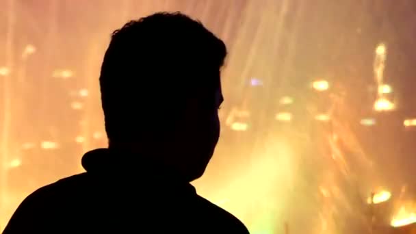 Joven se para cerca de una fuente iluminada y lo disfruta profundamente en la noche — Vídeos de Stock
