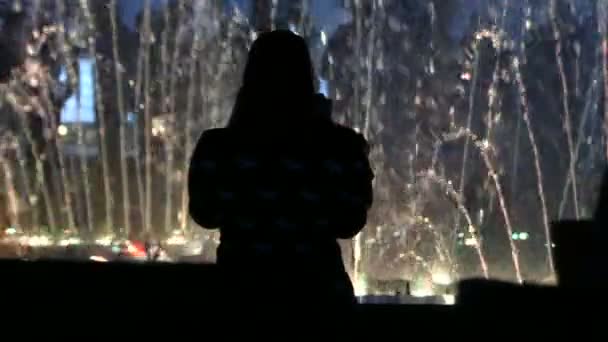 Femme dans un Hanky se tient près d'une fontaine éclairée et en profite la nuit — Video