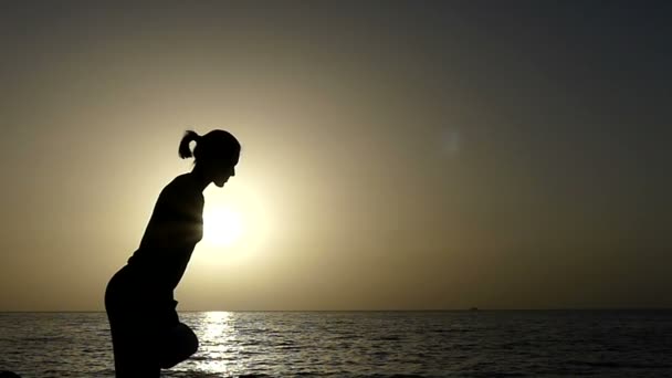 Jeune femme jette un tapis de yoga sur une côte rocheuse au coucher du soleil au ralenti — Video