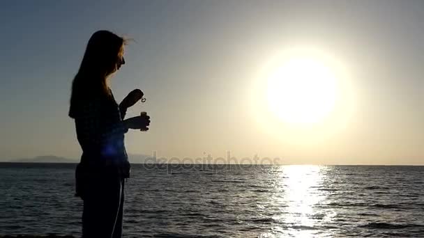 Mladá žena dělá mýdlové bubliny na pláži při západu slunce v pomalém pohybu — Stock video