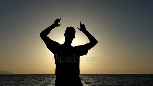 Dansları ve yavaş gün batımında sahil üzerinde jest gösterir numarası genç adam — Stok video