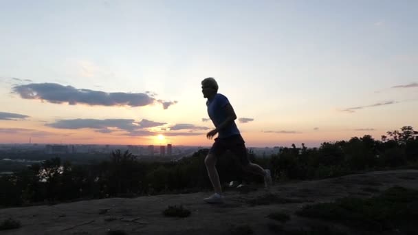 Молода людина біжить і стрибки переможно крокують на деякі горбистій місцевості на заході сонця в Slo-Mo — стокове відео