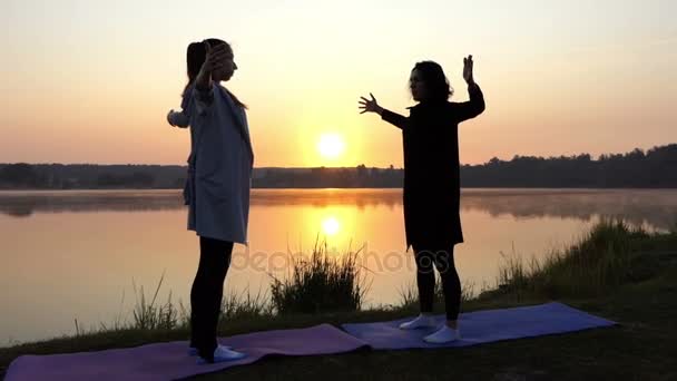 İki kadın bir kenara koymak eller bir göl kenarı Slo-mo gün batımında Yoga yaparken iken — Stok video