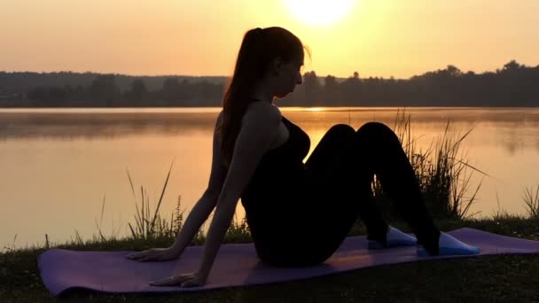 Una mujer embarazada se sienta y levanta su estómago en una estera en una orilla del lago en Slo-Mo — Vídeos de Stock