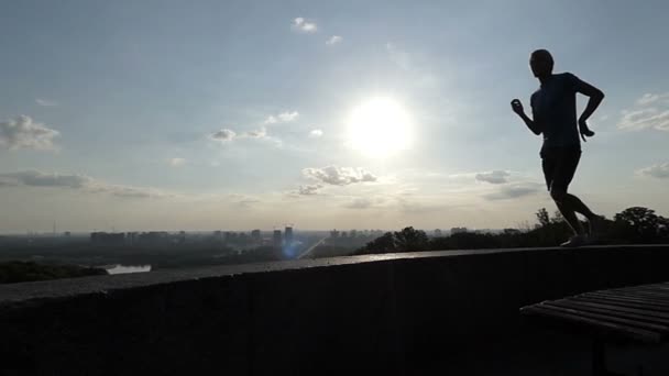 A fiatalember fut-ra egy kerítés, egy dombos területen vasbeton lemezek napnyugtakor a Slo-Mo — Stock videók