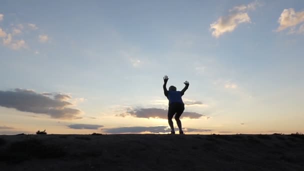 Молода людина високо стрибає і удари руками в гірському районі на заході сонця в Slo-Mo — стокове відео
