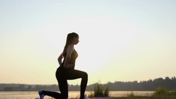 Jeune femme fait un squat divisé et une fente au coucher du soleil dans 4k — Video