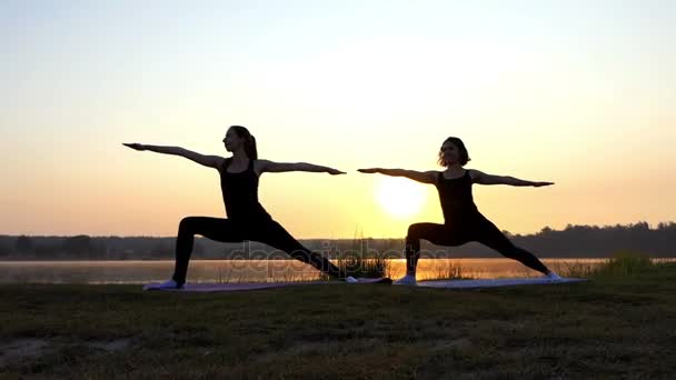 Dos jóvenes practican yoga en la pintoresca orilla del lago al atardecer — Vídeos de Stock