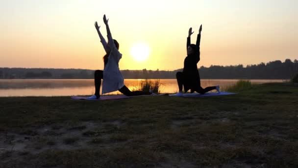 Super tramonto e donne che fanno guerriero 2 Esercizio di yoga su una riva del lago in Slo-Mo — Video Stock