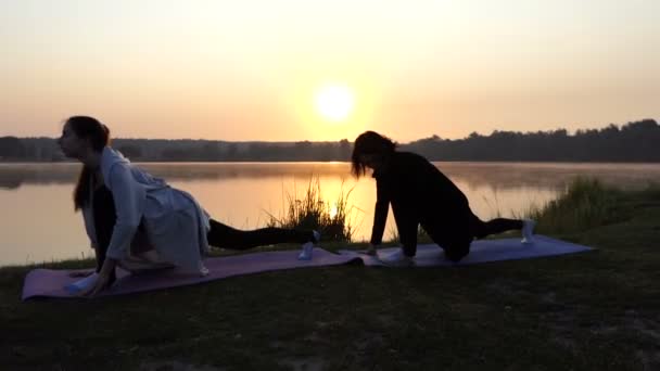 Дві жінки стенд на килимки і розтягнути на робити вперед випади на заході сонця в Slo-Mo — стокове відео