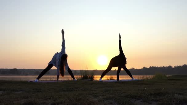 Esplêndido pôr do sol e mulheres fazendo exercício de ioga em um banco de lago em Slo-Mo — Vídeo de Stock