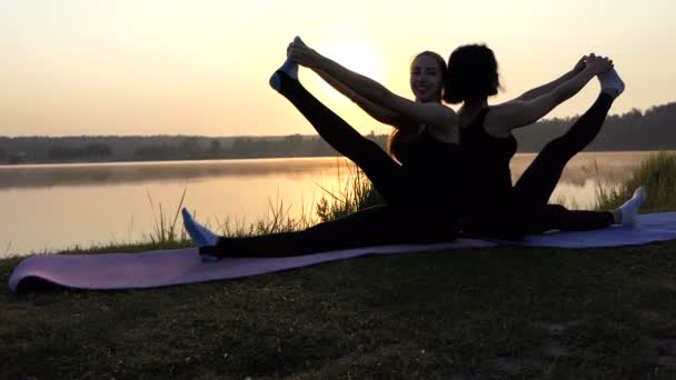 2 人の若い女性はスローモーションで日没でバックツー バックのマットの上に座ってヨガを練習します。 — ストック動画