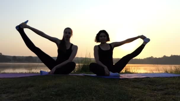 Dos chicas se sientan en las esteras, levantan las piernas aparte, sonríen, en una espléndida puesta de sol en Slo-Mo — Vídeo de stock