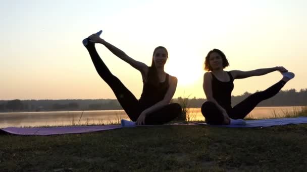 Dwie kobiety siedzą na matach, podnieść nogi na bok, relaks, wspaniały zachód słońca w Slo-Mo — Wideo stockowe