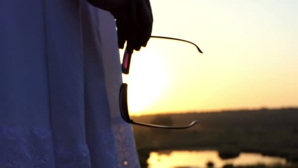 Una giovane donna bruna sta con gli occhiali da sole e guarda il tramonto a Slo-Mo — Video Stock