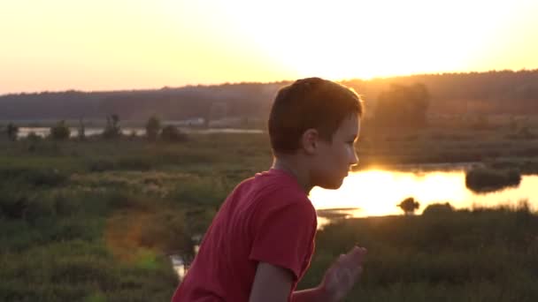 Petit garçon rit et joue Kung-Fu sur une rive du lac avec scirpe au coucher du soleil — Video