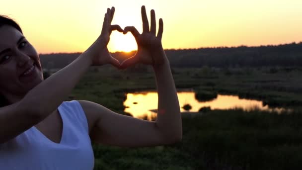 Jonge vrouw stuurt een hart gebaar naar haar vriendje bij zonsondergang in Slow Motion — Stockvideo