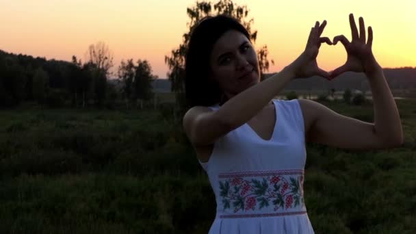 Mujer joven hace un gesto amoroso del corazón en una bonita puesta de sol en cámara lenta — Vídeo de stock