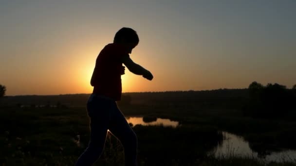 Niño pequeño lanza golpes de boxeo en una orilla del lago al atardecer en otoño en Slo-Mo — Vídeos de Stock