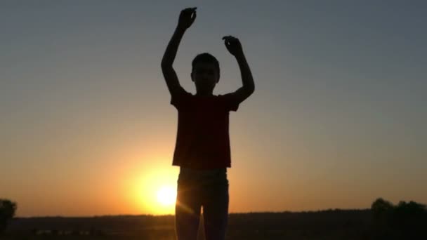 Μικρό αγόρι κάνει γύρο κινήσεις με τα χέρια του στο ηλιοβασίλεμα - εστίαση — Αρχείο Βίντεο