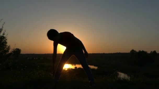 Kleine jongen doet fysieke oefeningen aan de oever van een meer bij zonsondergang in Slow Motion — Stockvideo