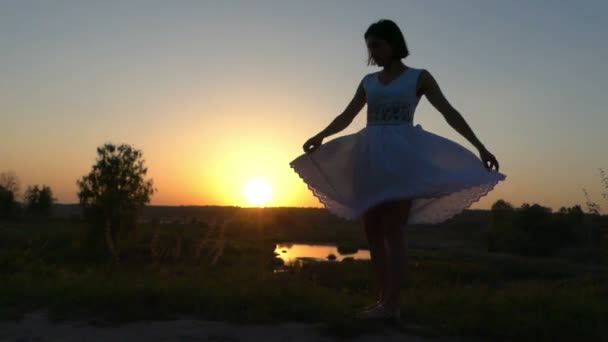 Junge Frau dreht den Saum ihres weißen Trachtenkleides bei schönem Sonnenuntergang — Stockvideo