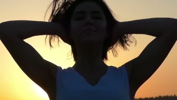 Eine Nahaufnahme einer schönen brünetten Frau, die ihre Haare direkt bei Sonnenuntergang setzt — Stockvideo