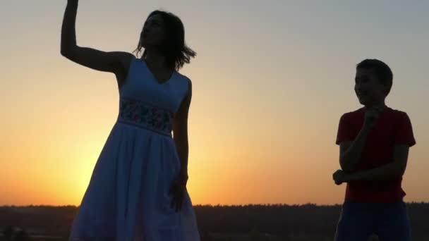 Een jongen en een jonge vrouw dans gelukkig bij zonsondergang — Stockvideo