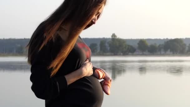 Una donna incinta divertente gioca con pantofole del bambino al tramonto — Video Stock