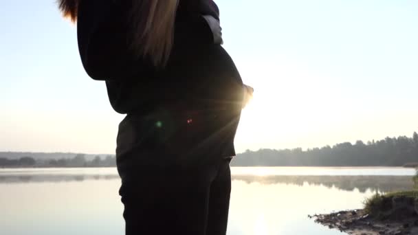 Mãos femininas Gok com chinelos de bebê na barriga grávida ao pôr do sol — Vídeo de Stock