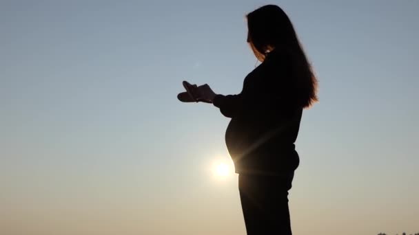 Una bella donna incinta gioca con pantofole del bambino al tramonto in autunno — Video Stock