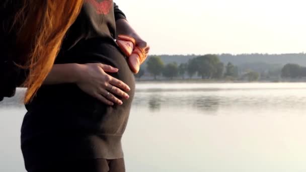 Eine fröhliche schwangere Frau spielt bei Sonnenuntergang im Herbst in Slo-mo mit Babypantoffeln — Stockvideo